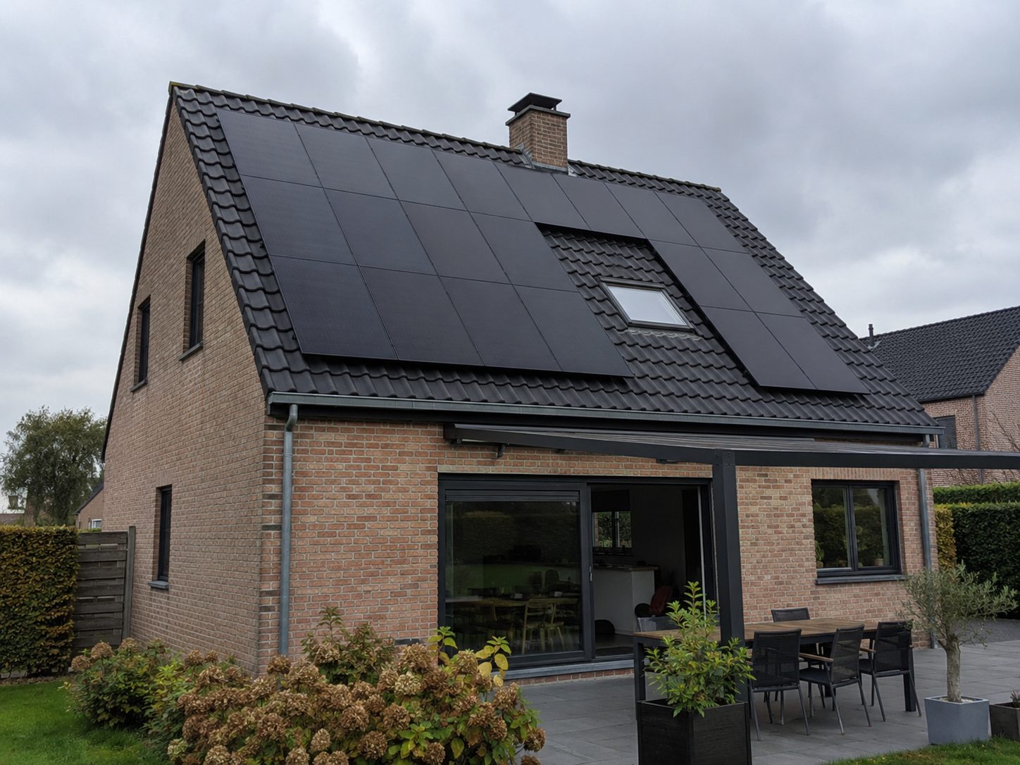 Zwarte JA Solar-zonnepanelen op het hellende pannendak van een bakstenen woning